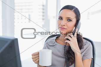 Serious secretary answering phone and drinking coffee