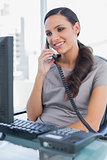Smiling secretary answering land line looking at computer screen