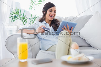 Laughing brunette buying online while having breakfast