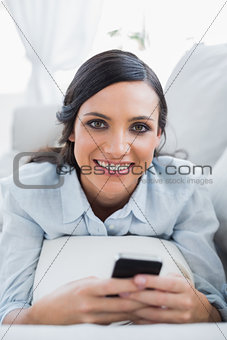 Cheerful pretty woman lying on the couch using her smartphone