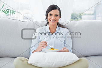 Pretty woman sitting on the couch crossing legs eating fruits