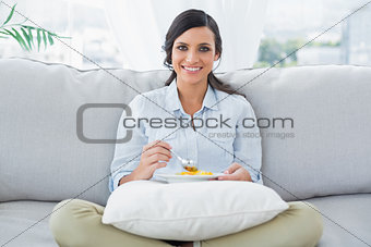 Woman sitting on the couch crossing legs eating fruits