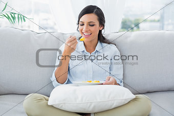 Cute woman sitting on the couch crossing legs eating fruits