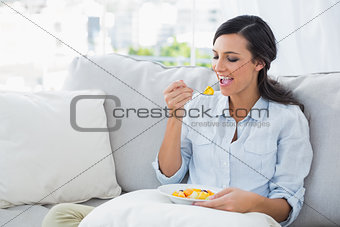 Woman relaxing on the sofa eating fruit salad