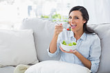 Cheerful woman relaxing on the sofa eating salad