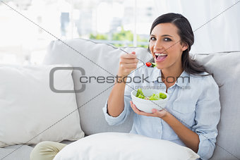 Cheerful woman relaxing on the sofa eating salad