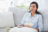 Astonished woman relaxing on the sofa eating popcorn