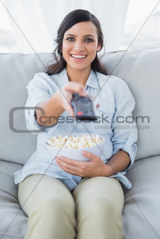 Cheerful pretty brunette watching tv and eating pop corn