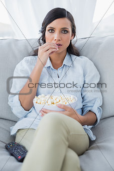 Concentrated pretty brunette watching tv and eating pop corn