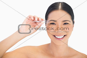 Cheerful natural model using tweezers for her eyebrow