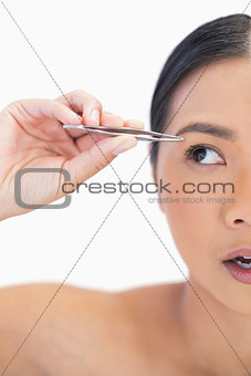 Half face of apprehensive natural woman using tweezers
