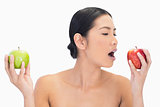 Black haired model holding apples in both hands eating the red one