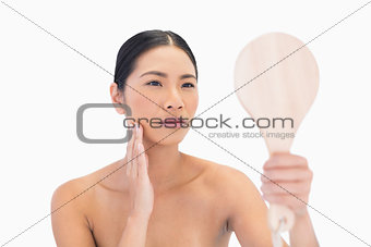 Natural dark haired model holding mirror touching her cheek