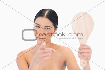 Dark haired young model holding mirror pointing out at camera