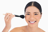 Cheerful dark haired woman applying powder on her face