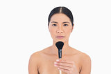 Unsmiling dark haired woman holding powder brush in front of her