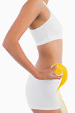 Profile of female slender body in sport underwear holding orange