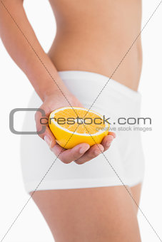 Toned female body holding half orange