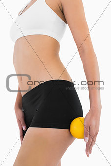 Female slender body with sport underwear holding orange