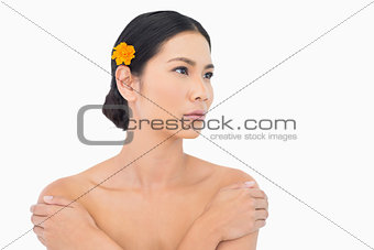 Thoughtful model with orange flower in hair touching her shoulders