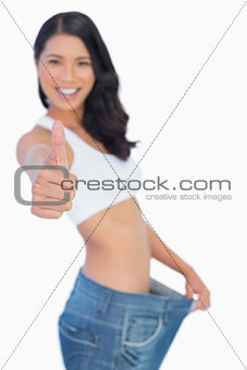 Victorious woman holding her too big pants thumbs up