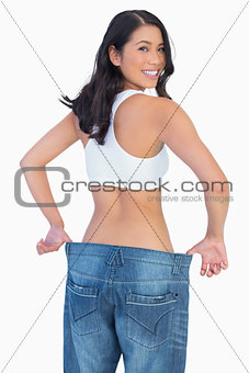 Woman holding her too big jeans smiling at camera