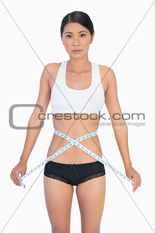 Serious slim woman measuring her waist