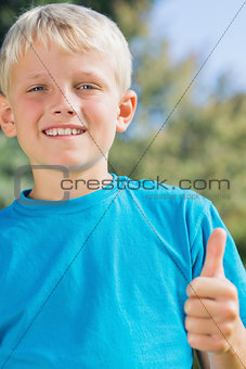 Little blonde boy smiling at camera giving thumbs up