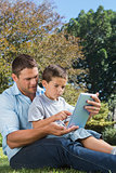 Dad and son playing with a tablet pc in a park