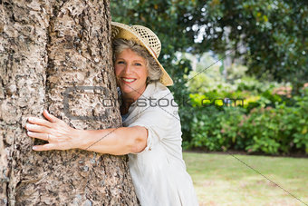 Retired woman hugging a tree smiling at camera