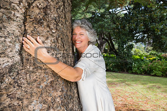 Smiling older woman hugging a tree