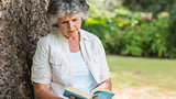 Cheerful mature woman reading book sitting on tree trunk
