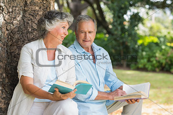 Older couple reading books together sitting on tree trunk