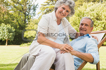 Happy mature woman sitting on her husband on deck chair