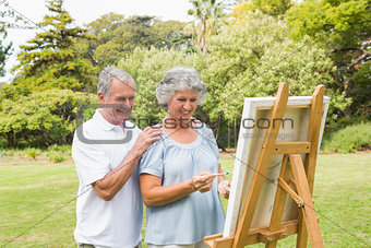 Cheerful retired woman painting on canvas with husband
