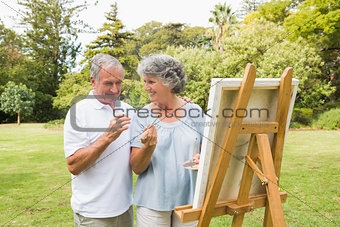 Smiling retired woman painting on canvas with husband