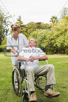 Happy man sitting in a wheelchair talking with his nurse pushing him