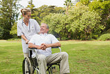 Smiling man sitting in a wheelchair talking with his nurse pushing him