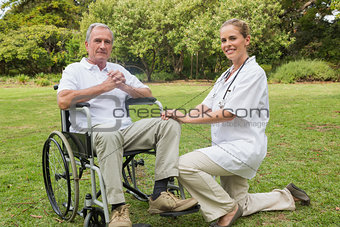 Cheerful man in a wheelchair with his nurse kneeling beside
