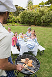 Happy extended family having a barbecue being cooked by father in chefs hat