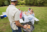 Father in chefs hat and apron cooking barbecue for his family