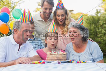 Cheerful extended family watching girl blowing out birthday candles