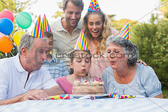 Happy extended family watching girl blowing out birthday candles