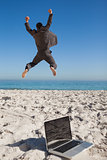 Victorious businessman in suit jumping leaving his laptop