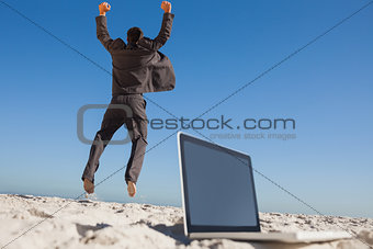 Victorious businessman jumping leaving his laptop