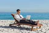 Young businessman lying on a deck chair with his laptop