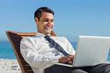 Happy young businessman on a deck chair using his computer