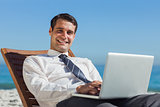 Cheerful young businessman lying on a deck chair with his computer