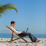 Young businessman on his beach chair using his laptop