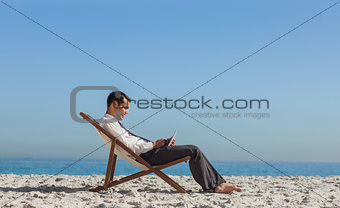 Young businessman resting on his deck chair using his tablet